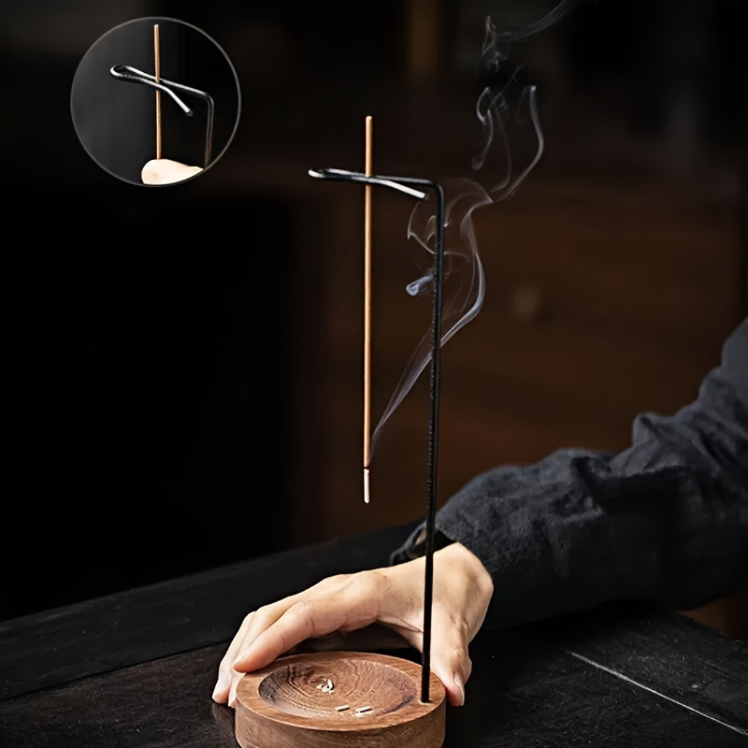 Hand holding a wooden incense burner with two sticks emitting smoke against a dark background