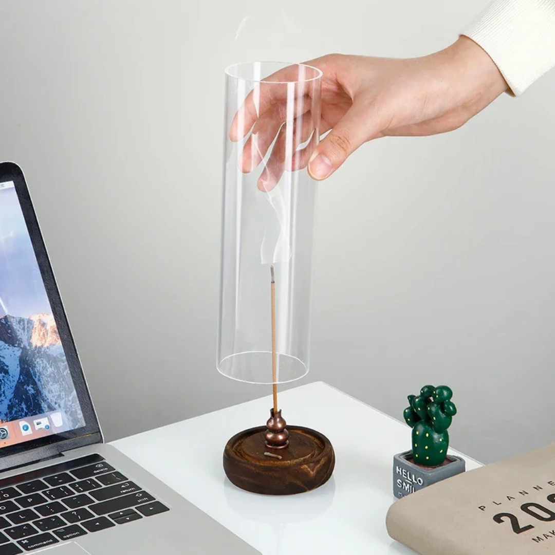 Hand holding a clear cylindrical object over a wooden base with a laptop on a desk.