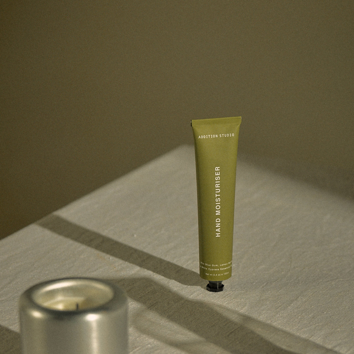 Addition Studio Blue Gum and Lemon Myrtle Hand Cream 100mL styled on linen beside a candle