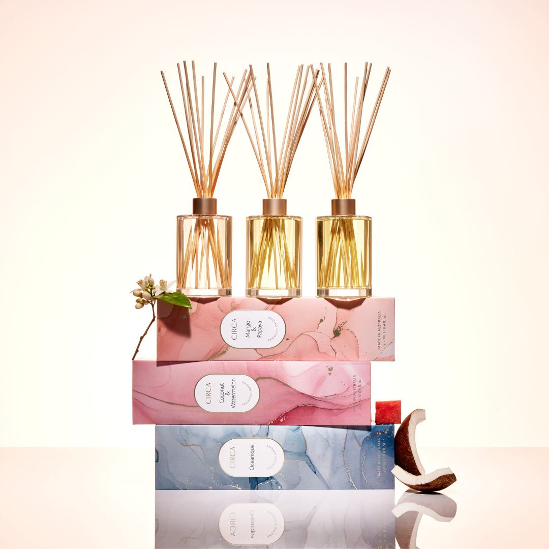 Circa Home reed diffusers in elegant glass bottles, displayed on top of beautifully designed packaging boxes. Scents include Mango & Papaya, Coconut & Watermelon, and Oceanique, creating a luxurious aromatic experience for the home. Available at The Gift Company.