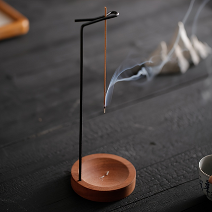 Incense stick on a wooden stand with smoke on a dark surface