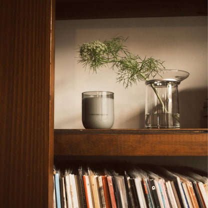 Studio Milligram Ultra Violet glass candle arranged on wooden bookshelf alongside vase